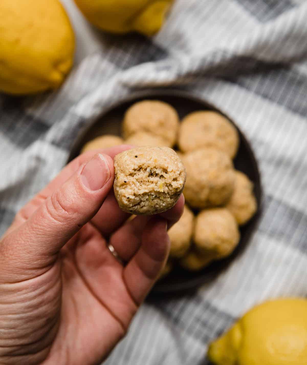 A hand holding a Lemon Protein Bite with a bite taken out of the protein ball.
