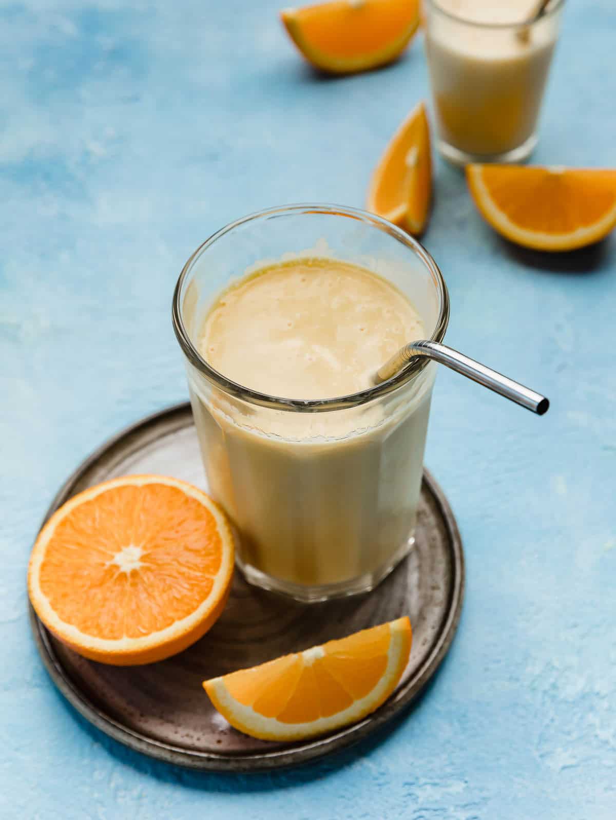 A homemade Orange Julius Recipe in a large glass cup with a stainless steel straw in the cup, on a light blue background.