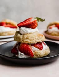 A classic strawberry shortcake with a flaky biscuit on a black plate.