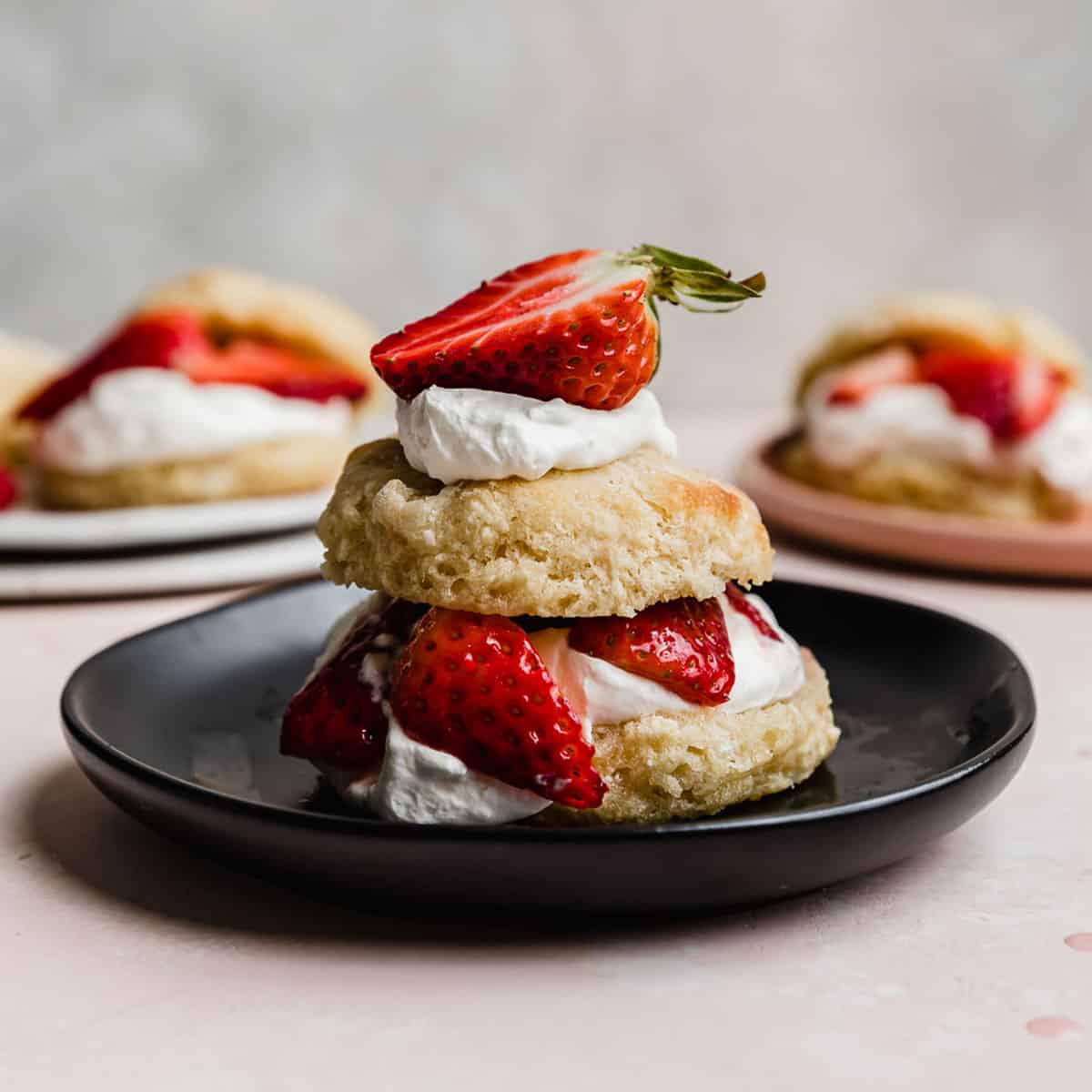 A classic strawberry shortcake with a flaky biscuit on a black plate.