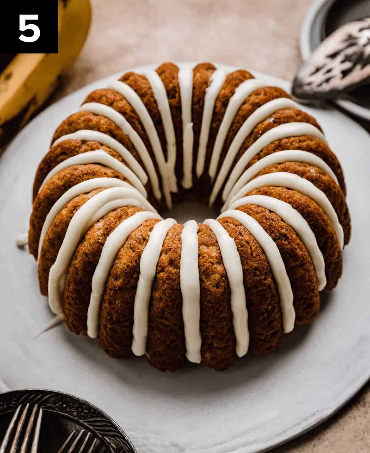 A cream cheese glazed Banana Bread Bundt Cake on a white cake plate.