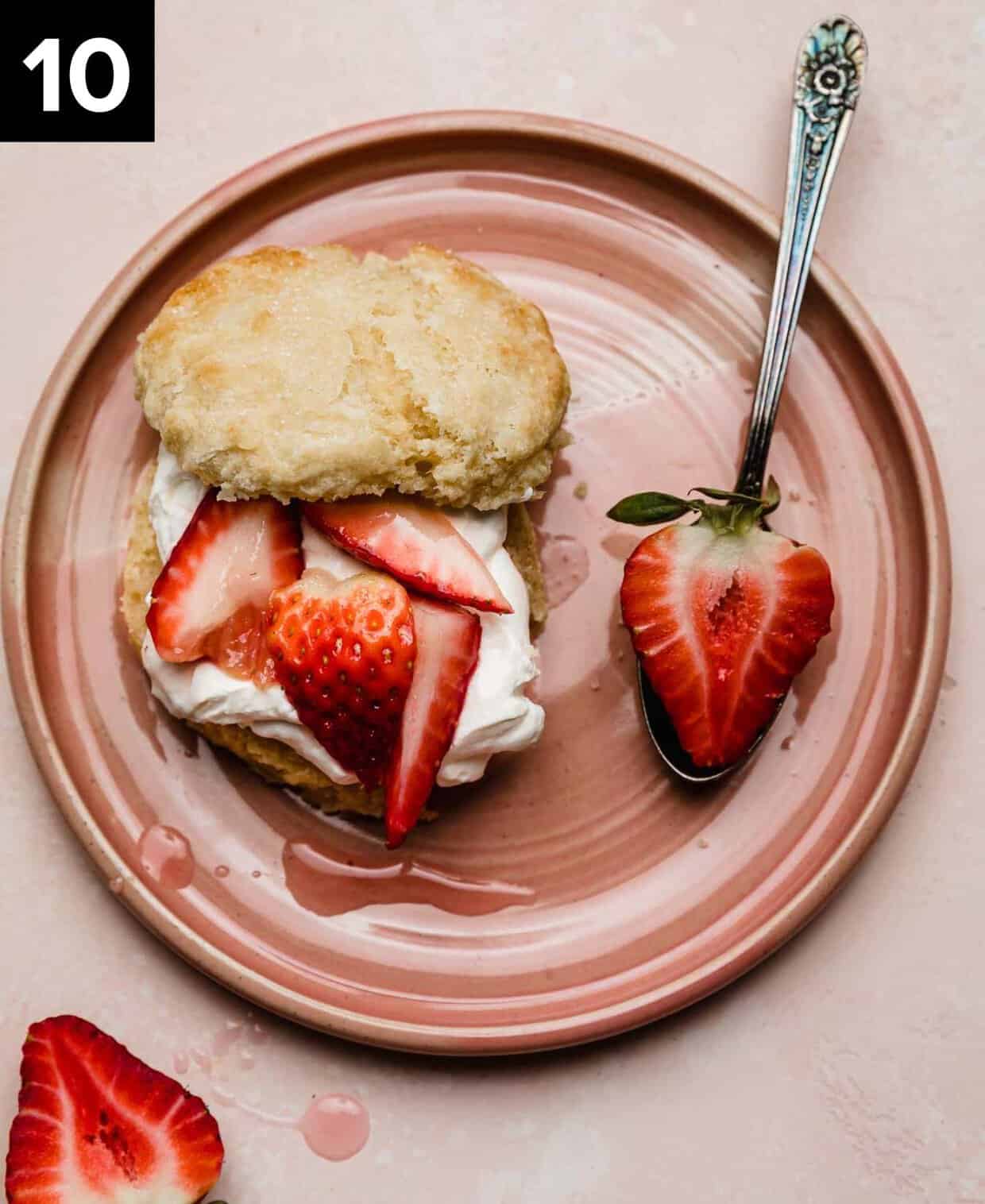 A classic Classic Strawberry Shortcake on a pink plate featuring a flaky biscuit topped with whipped cream and quartered strawberries.