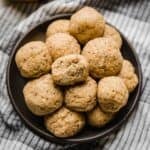 A bite taken out of a Lemon Protein Ball that's stacked on a black plate with other lemon poppy seed protein balls.