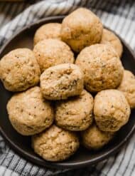 A bite taken out of a Lemon Protein Ball that's stacked on a black plate with other lemon poppy seed protein balls.