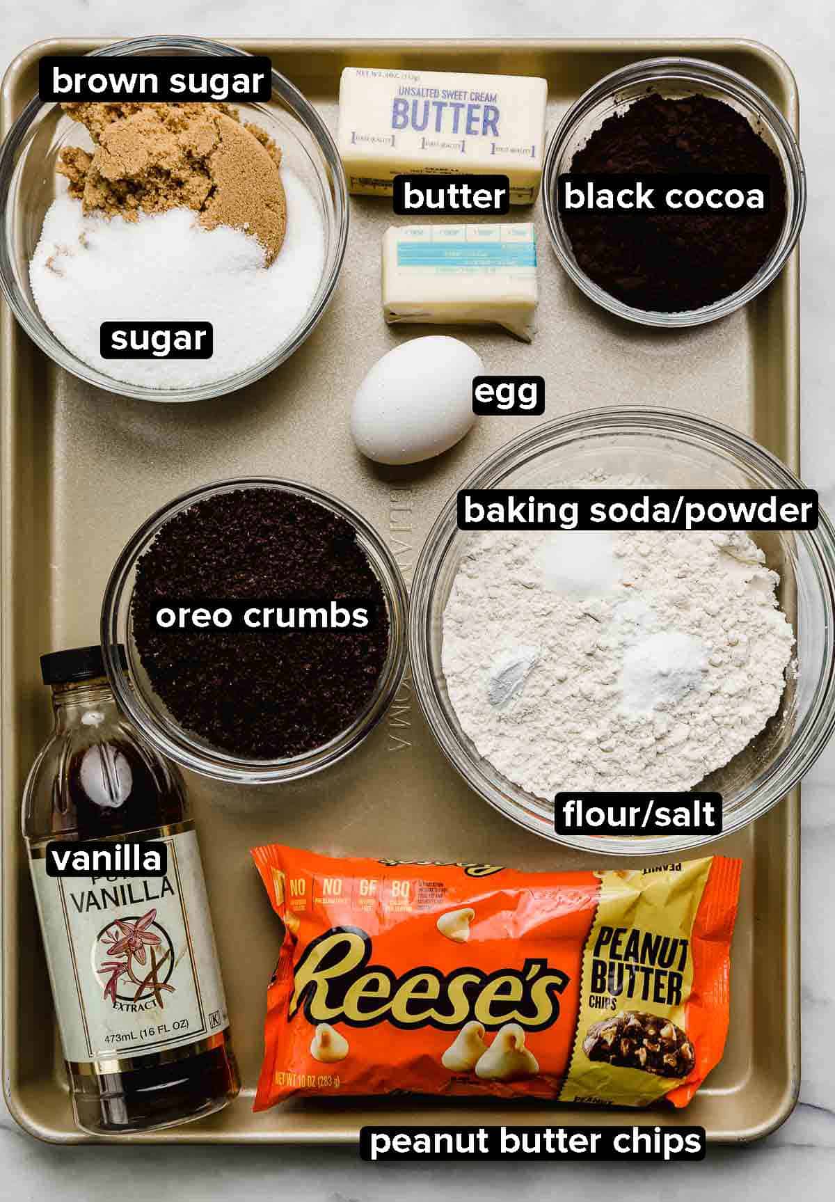 Peanut Butter Oreo Cookie ingredients on a gold baking sheet: peanut butter chips, flour, salt, baking powder and soda, vanilla, butter, eggs, and sugars.