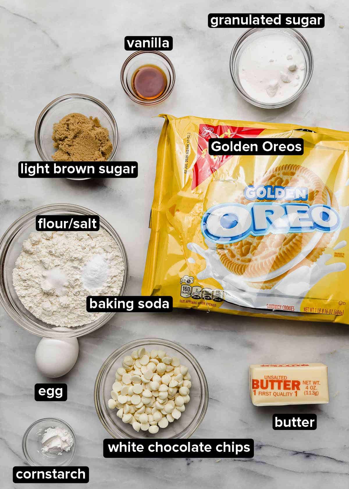 Crumbl Golden Oreo cookie recipe ingredients on a white marble surface: golden Oreos, flour, white chocolate chips, egg, butter, salt, baking soda, vanilla, and sugars.