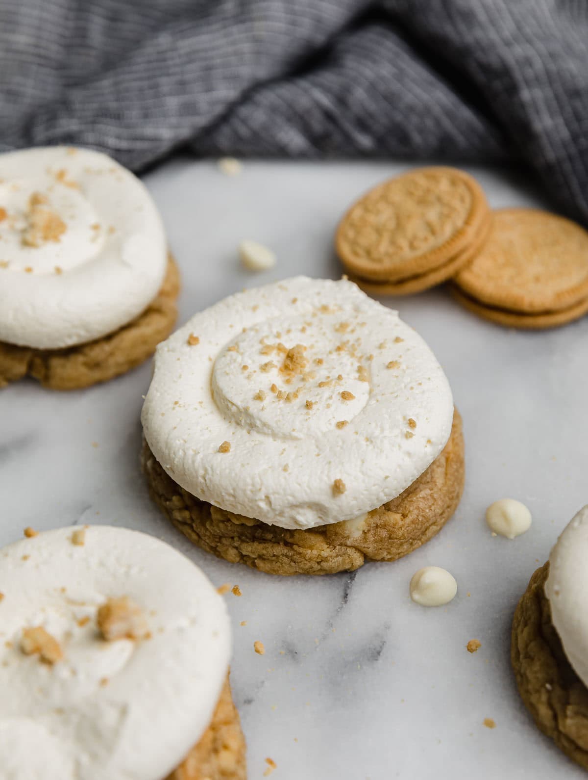 White frosting topped Golden Oreo Cookies with white chocolate chips on a white marble surface.