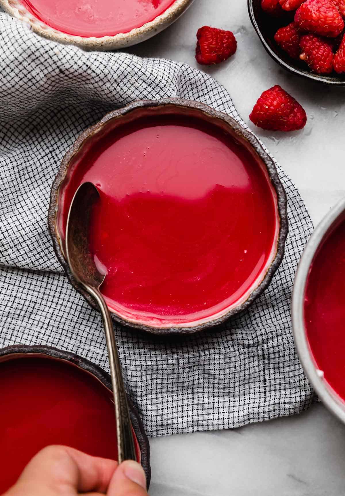A black rimmed bowl filled with brightly colored Cold Raspberry Soup on a small checkered linen napkin.