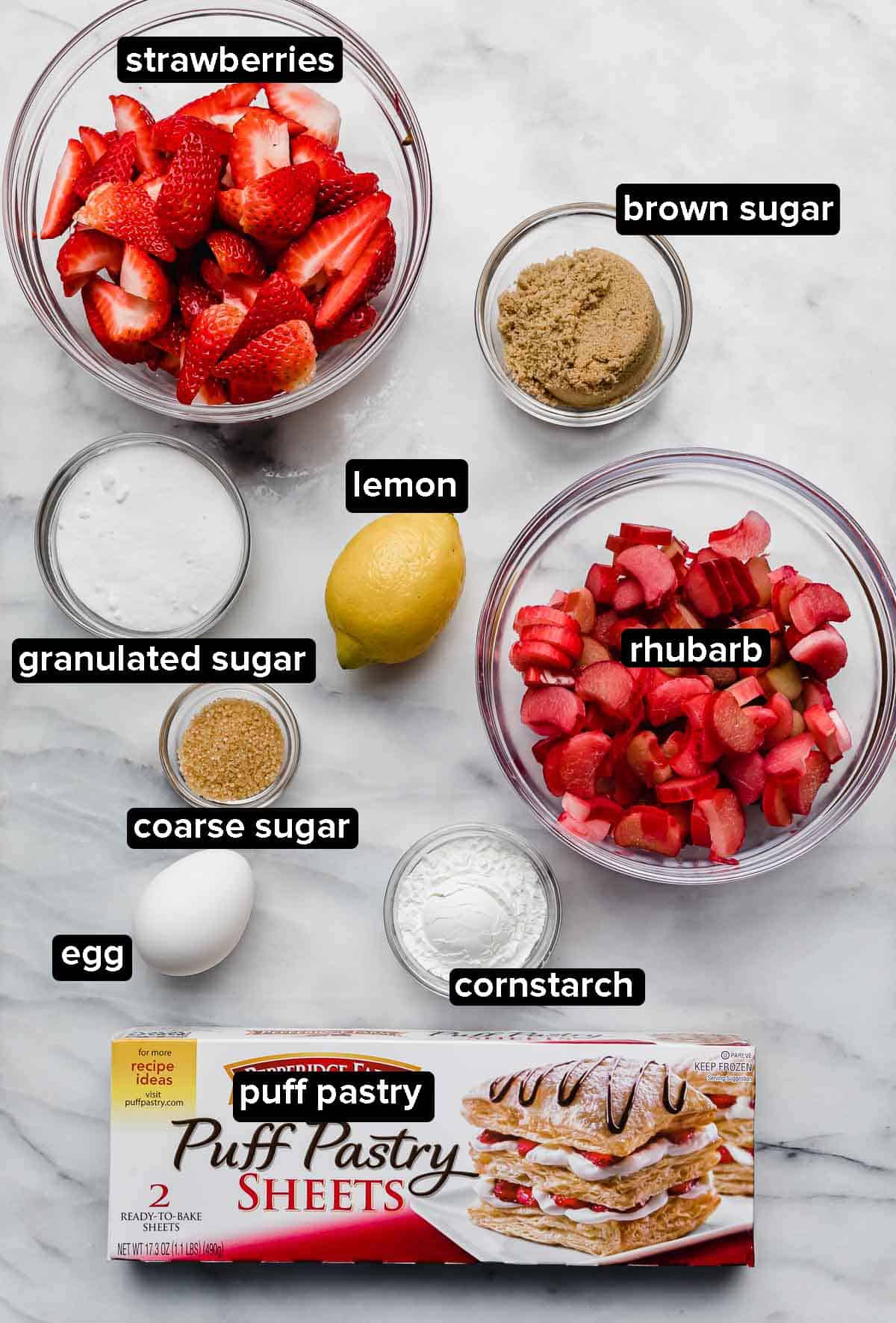 Ingredients used to make a Rhubarb Strawberry Galette recipe: fresh strawberries, rhubarb, puff pastry sheets, egg, sugar, cornstarch, and lemon.