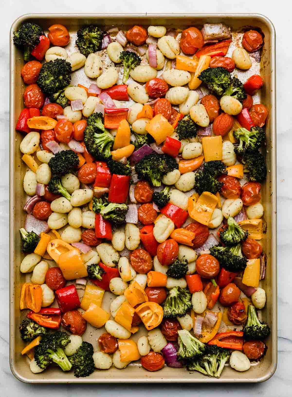 A baking sheet filled with gnocchi and vegetables including broccoli, peppers, tomatoes, and red onion.