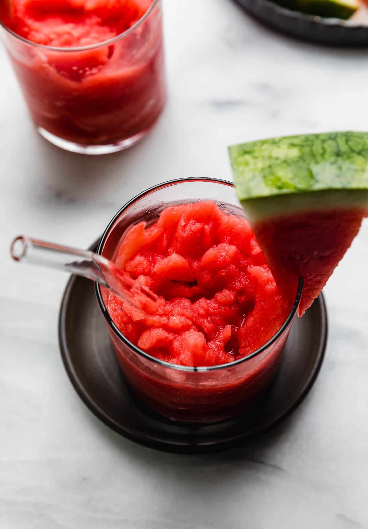 Overhead photo of bright red watermelon slushie in a glass cup on a black plate.