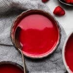 Cold Raspberry Soup in a black bowl with a spoon in the bowl and fresh raspberries near the bowl.
