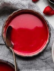 Cold Raspberry Soup in a black bowl with a spoon in the bowl and fresh raspberries near the bowl.