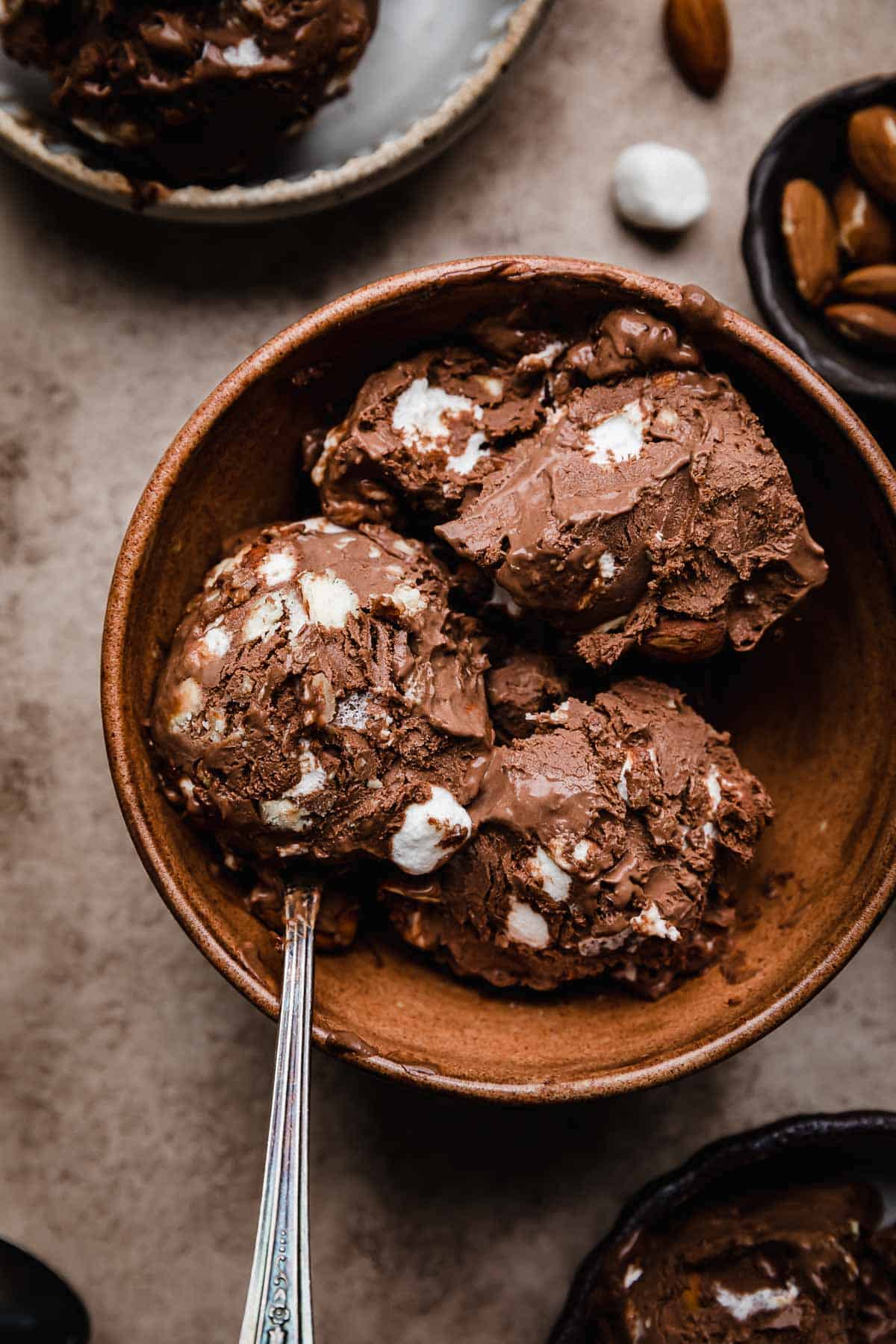 Rocky Road Ice Cream Recipe scooped into a brown bowl with a spoon scooping some of the marshmallow and almond chocolate ice cream.