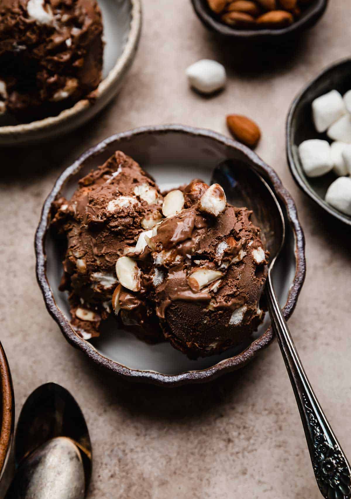 Two scoops of Rocky Road Ice Cream in a black rimmed bowl on a light brown textured background.