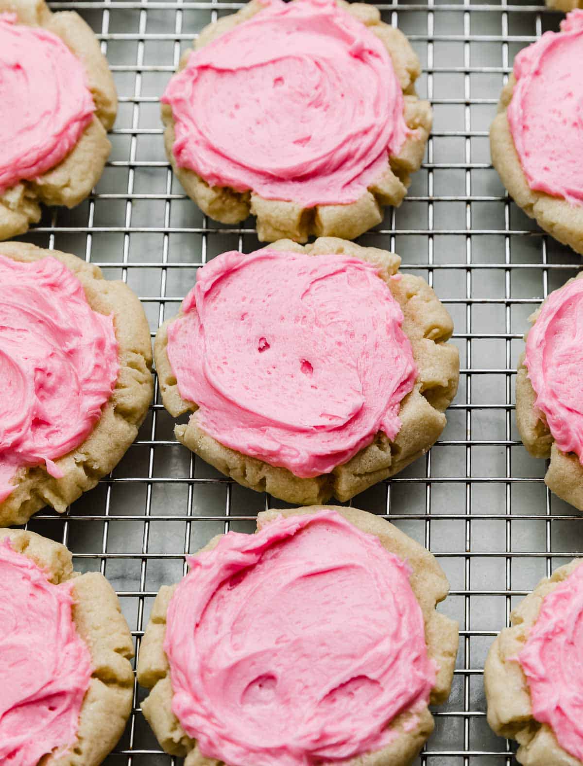 Swig sugar cookies on a wire cooling rack, each round cookie covered with a pink sour cream frosting.