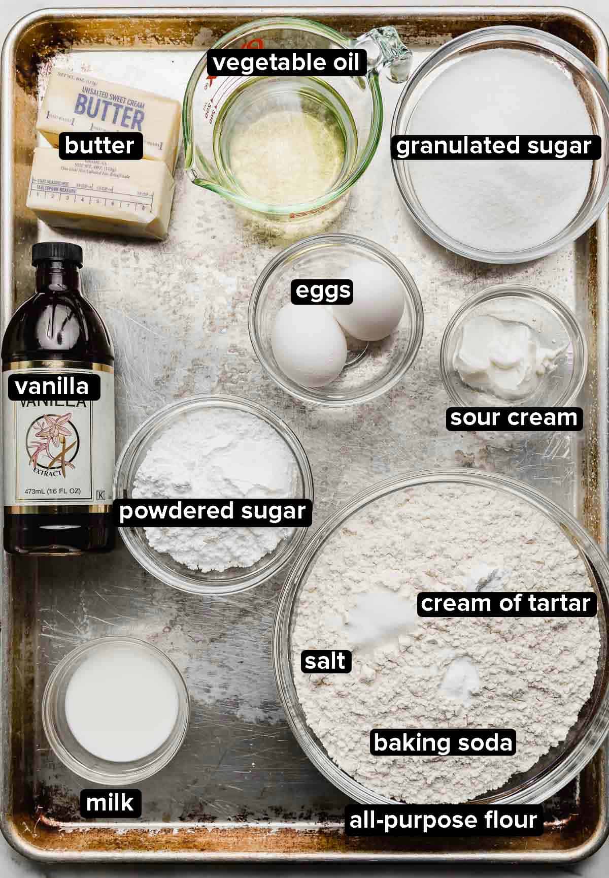 Swig Sugar Cookie Recipe ingredients portioned into glass bowls on a metal baking sheet: butter, oil, sugar, flour, leavening agents, salt, sour cream, vanilla, and eggs.