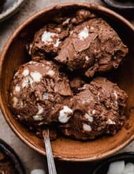 3 scoops of mini marshmallow and toasted almonds mixed into a chocolate custard ice cream base (rocky road ice cream), scooped into a brown bowl.