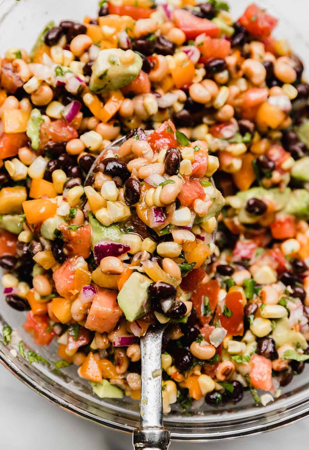 A large glass bowl filled with the best cowboy caviar (Texas Caviar) recipe with a large spoon scooping out the fresh dip.