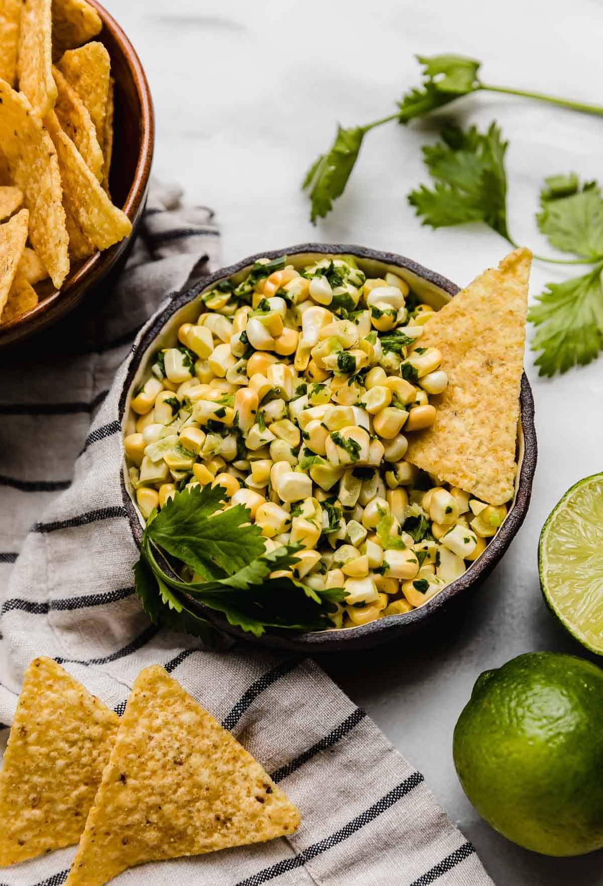 A black bowl filled with Fresh Corn Salsa with jalapeño and cilantro on a white background.