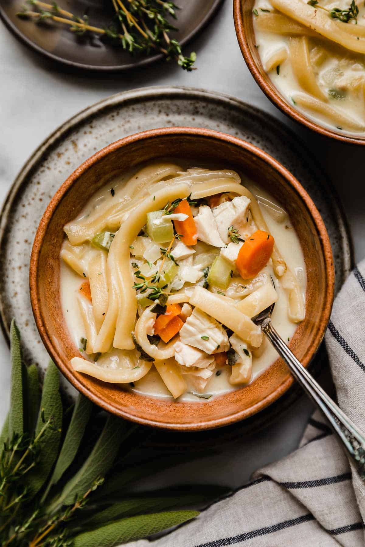 Close up photo of Creamy Chicken Noodle Soup topped with fresh thyme in a brown bowl.