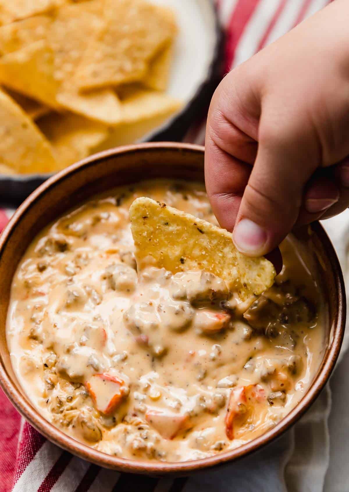 Cream Cheese Sausage Rotel Dip made in a crock pot, with a hand scooping a tortilla chip into the Rotel dip.