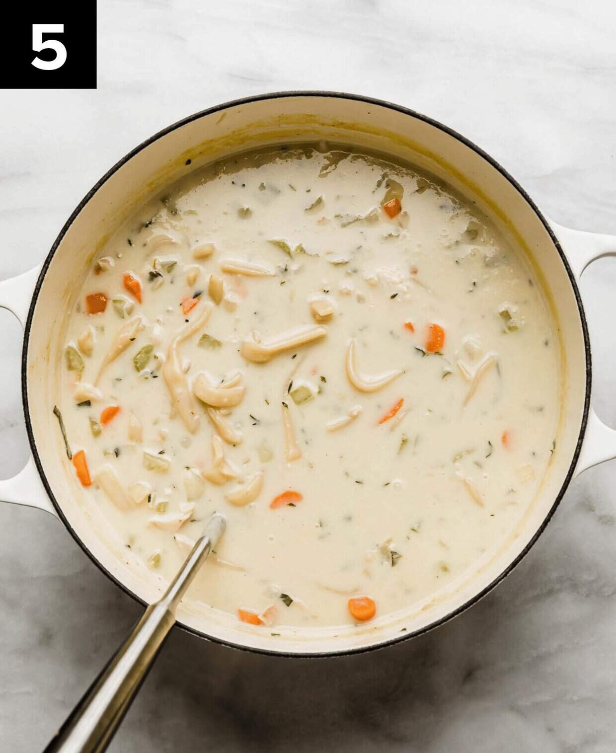 A white Dutch oven filled with the best Creamy Chicken Noodle Soup Recipe made with grandma's wide egg noodles and fresh herbs.
